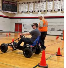 A person on a peddle cart wearing a virtual reality googles next to a COP member